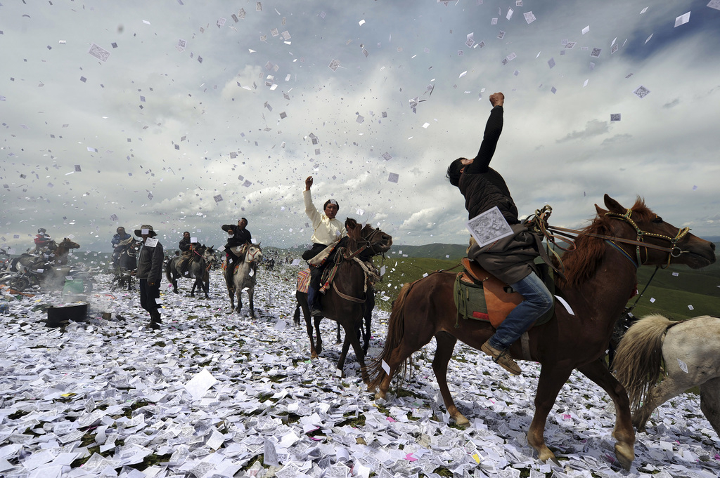 Tibetanen te paard gooien gebeden in de lucht, terwijl ze zich verzamelen voor het gebedenfestival Wei Sang. – © Miguel Vidal / Reuters