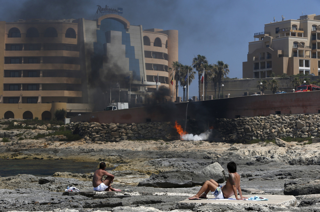 Zonnebadende toeristen op Malta kijken naar een brand in het Radisson Blu hotel in St Julian's, in de buurt van Valletta. – ©  Zammit Lupi / Reuters