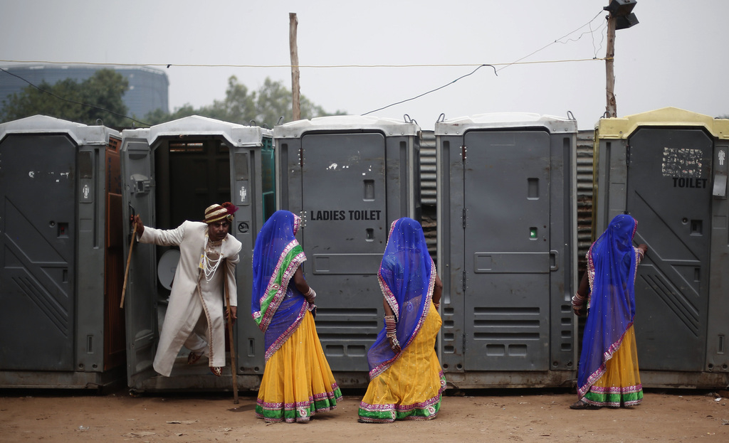 Een bruidegom komt uit een toilet terwijl bruiden staan te wachten bij een massabruiloft voor gehandicapten in New Delhi. – © Adnan Abidi / Reuters